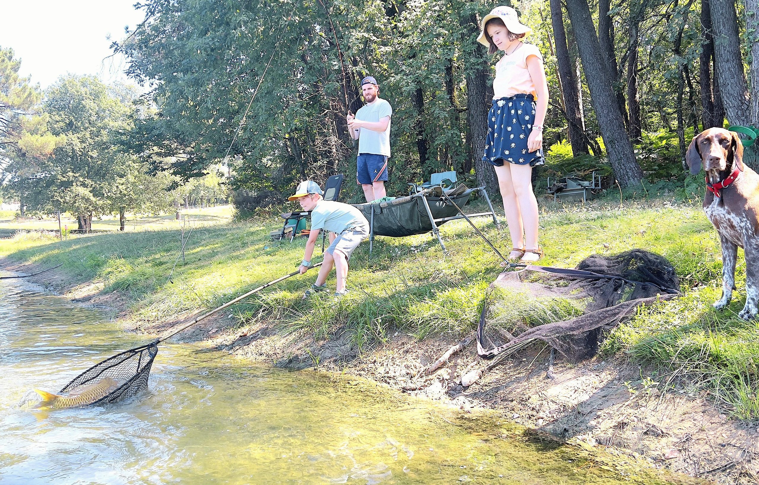 Père avec ses enfants et leur chien pêchant une carpe à l’épuisette